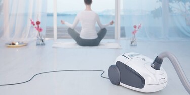 Sieviete nodarbojas ar jogu ar savu Electrolux Ultra Silencer putekļu sūcēju priekšplānā